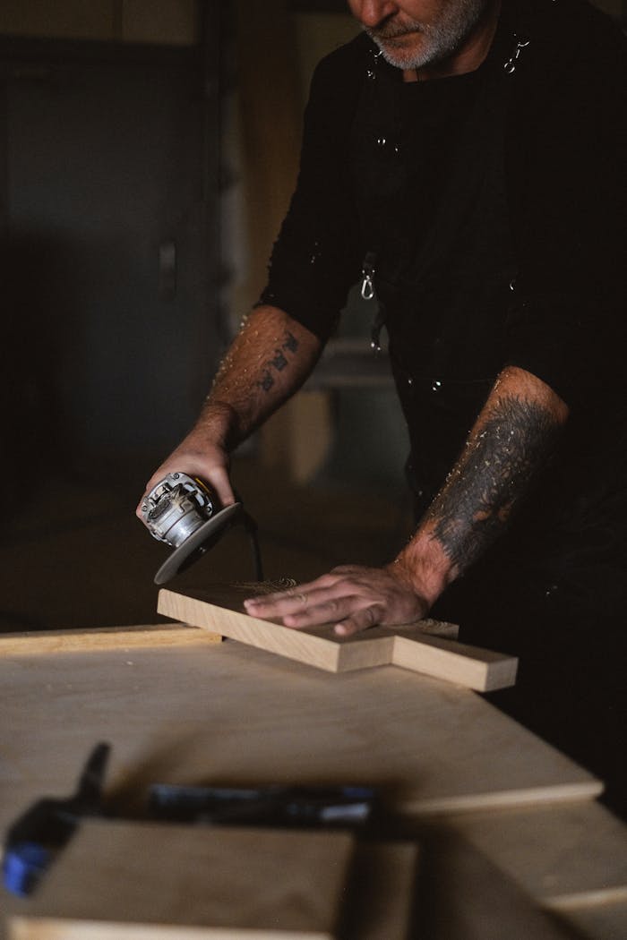 A focused craftsman polishing wood with a grinder in his workshop, showcasing professional skill and technique.
