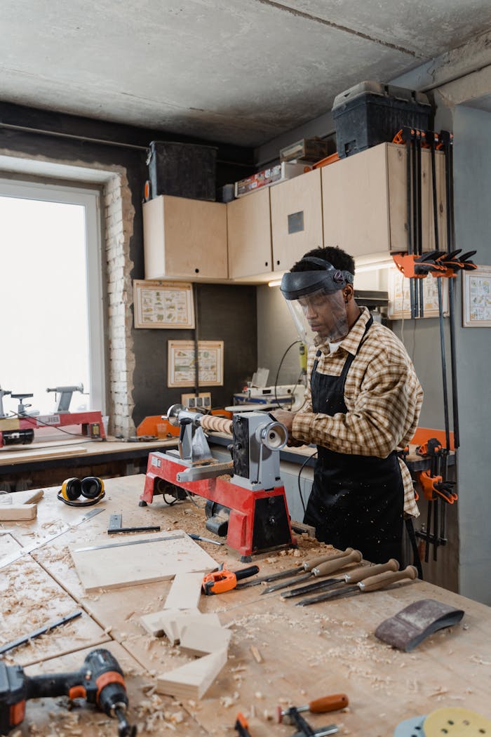 Woodworker using lathe surrounded by tools and sawdust in a workshop.