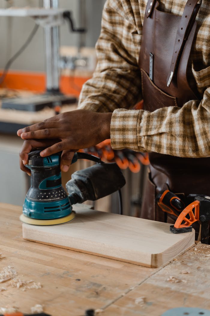 Person sanding a wooden board in a workshop using an electric sander.